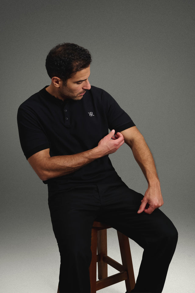 Rflx Reflection Polo in black, seated, leaning forward, adjusting the sleeve cuff