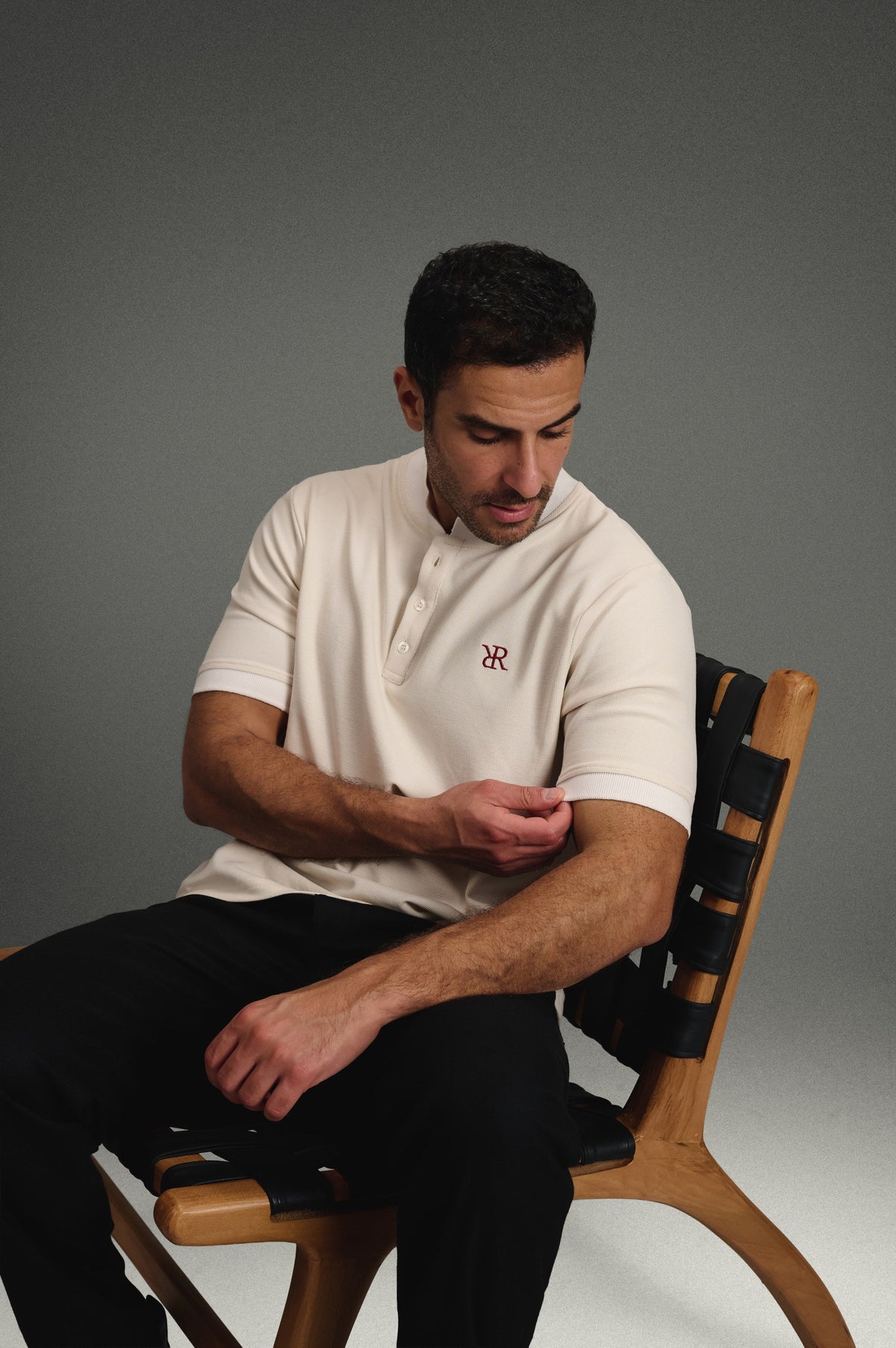 Rflx Reflection Polo in cream with white ribbed trim, seated, adjusting the sleeve cuff