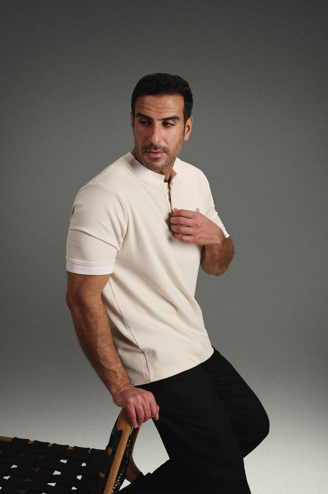 Rflx Reflection Polo in cream with white ribbed trim, standing, hand at the placket, looking away