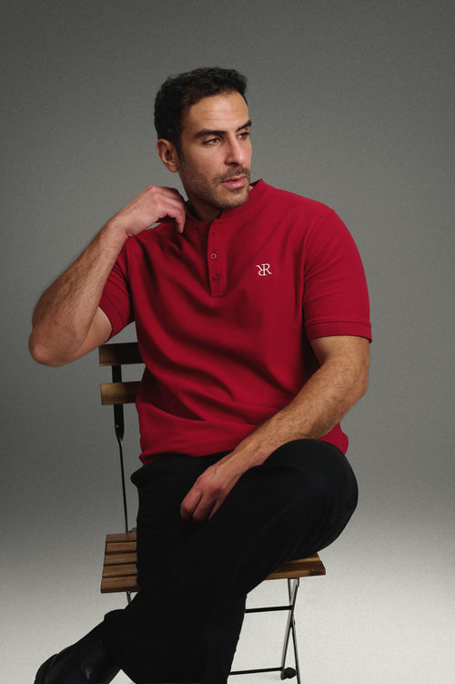 Rflx Reflection Polo in crimson, seated on a stool, arm resting on the backrest