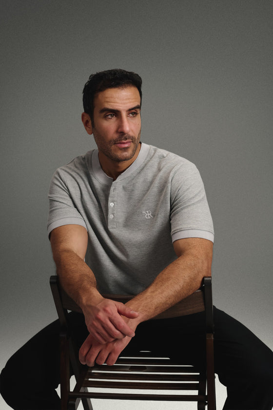 Rflx Reflection Polo in heather grey with lilac ribbed trim, seated, forearms resting on the chair back