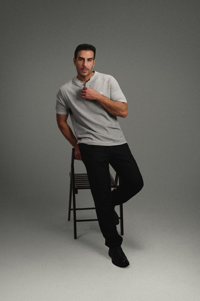 Rflx Reflection Polo in heather grey with lilac ribbed trim, standing with one foot on a stool, hand at the placket