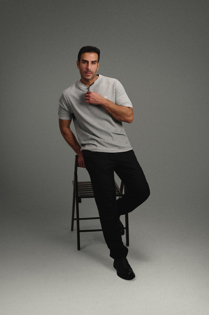 Rflx Reflection Polo in heather grey with lilac ribbed trim, standing with one foot on a stool, hand at the placket
